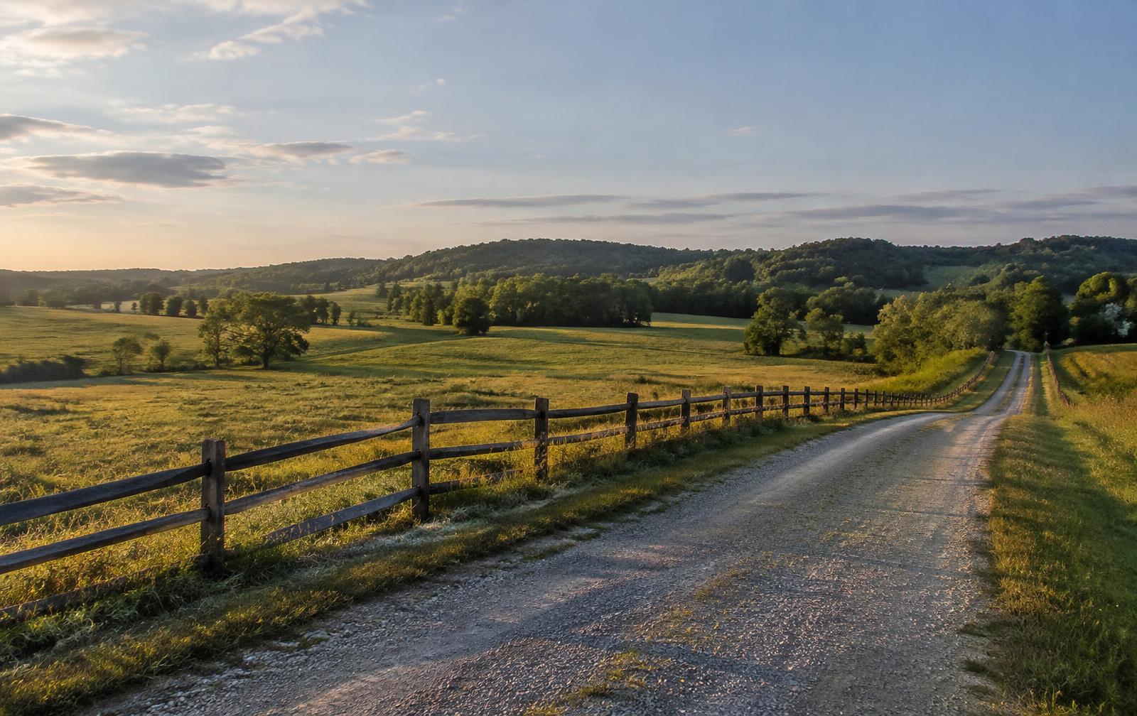 Gravel road along a wooden fence through rolling farmland